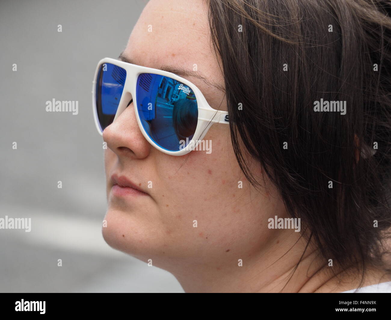 pensive dark haired female wearing blue tinted reflective sunglasses with white frames Stock Photo