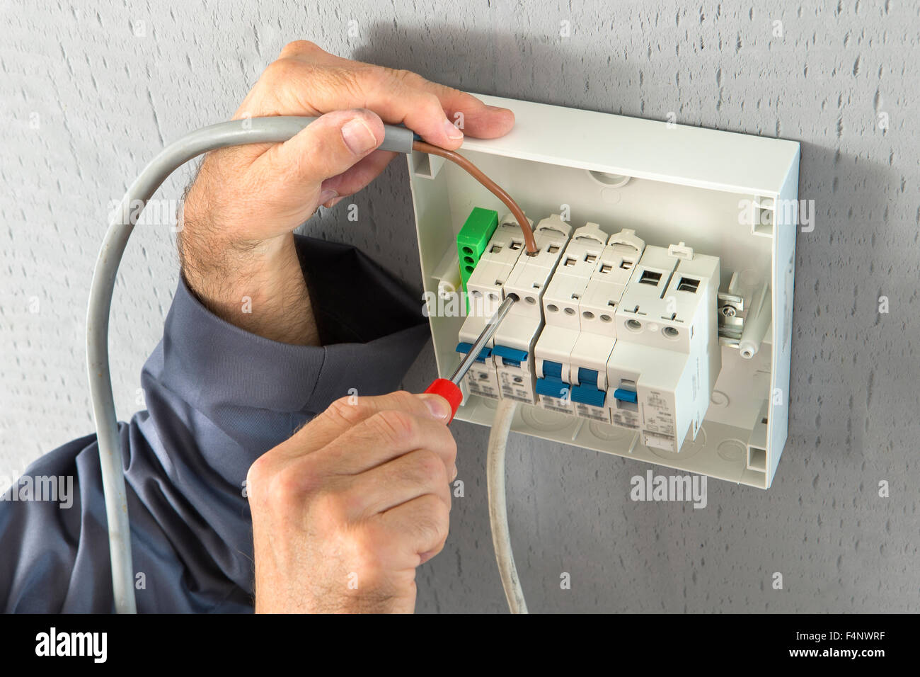electrician builder engineer screwing equipment in fuse box - Stock Image