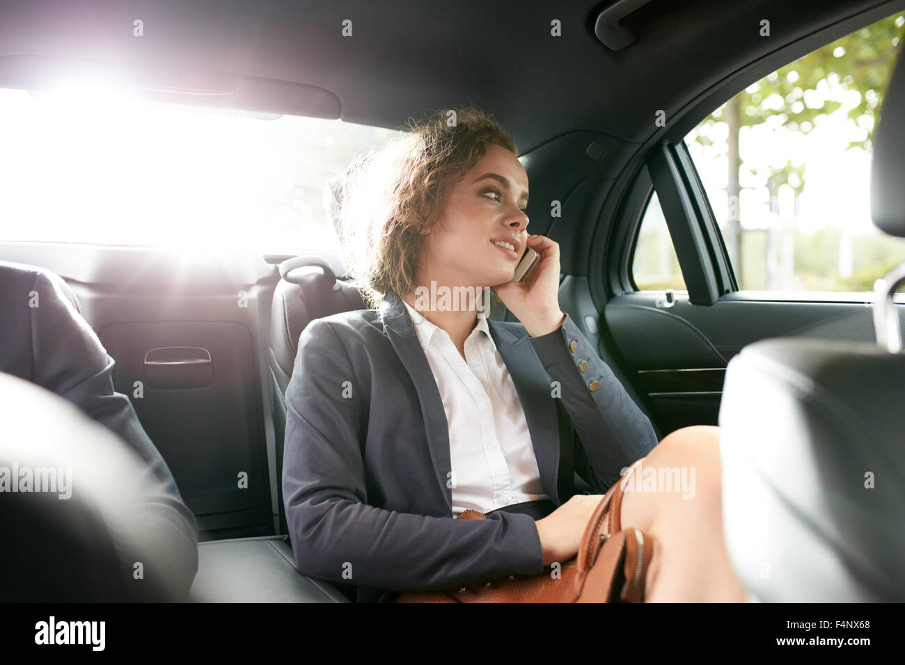 Shot of happy young businesswoman traveling to work in the luxury car on the back seat and talking by phone. Stock Photo