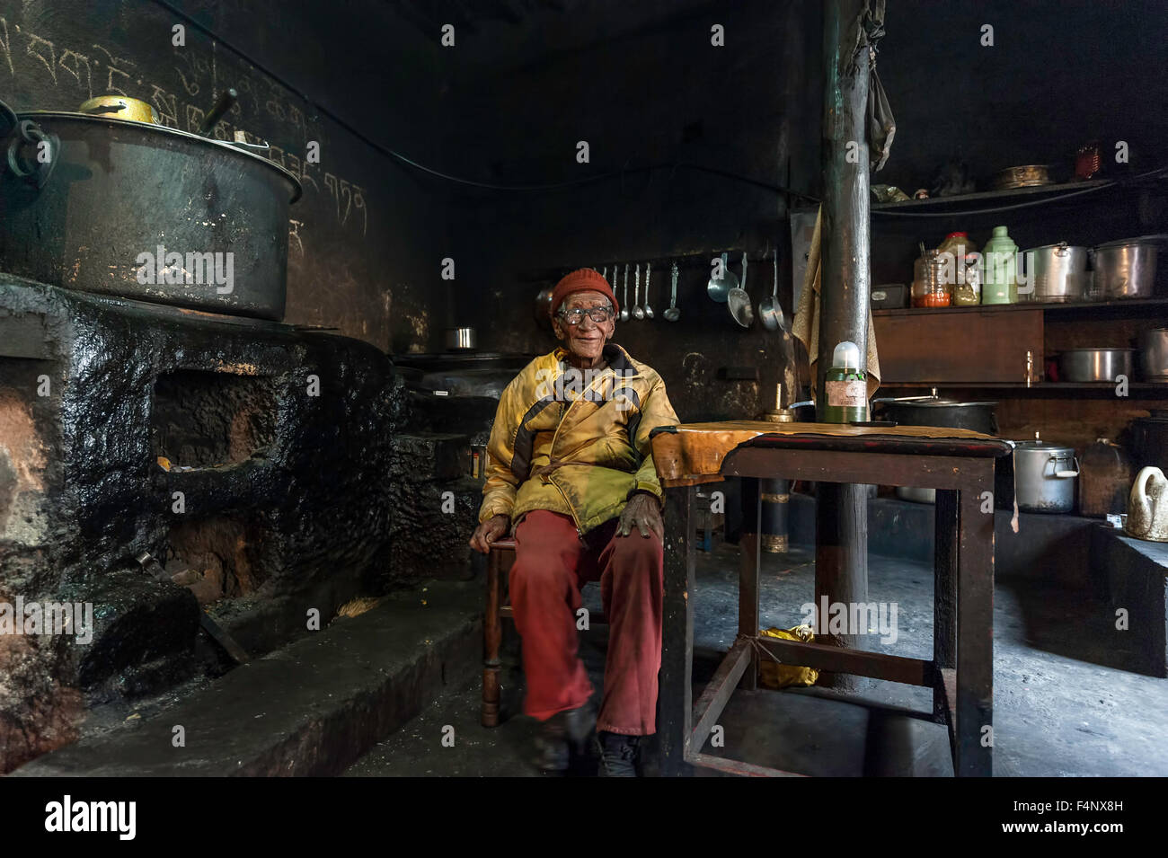 Old Monk is sitting in kitchen next to the fire. Stock Photo