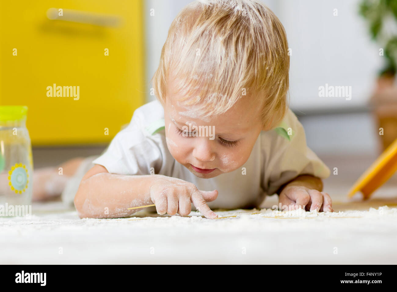 Little child laying on very messy kitchen floor, covered in white baking flour Stock Photo