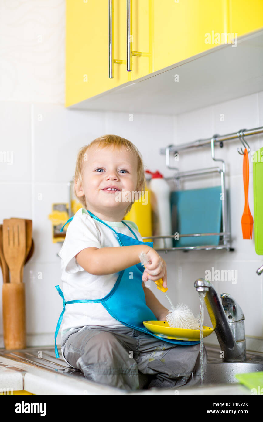 Kid boy washing dishes and having fun in the kitchen Stock Photo