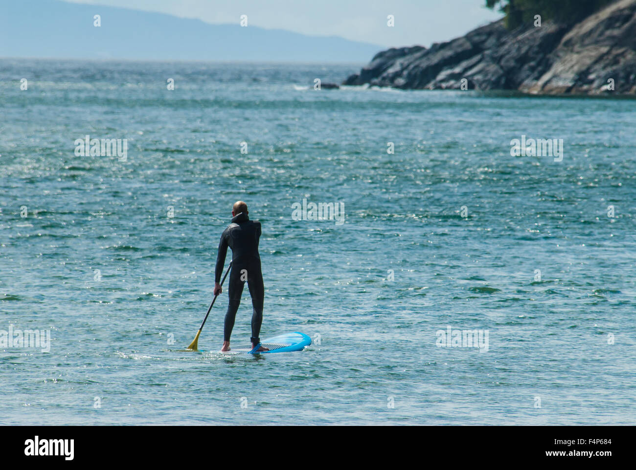 A standup paddleboarder in a wet suit paddling at China Beach on Vancouver Island Stock Photo
