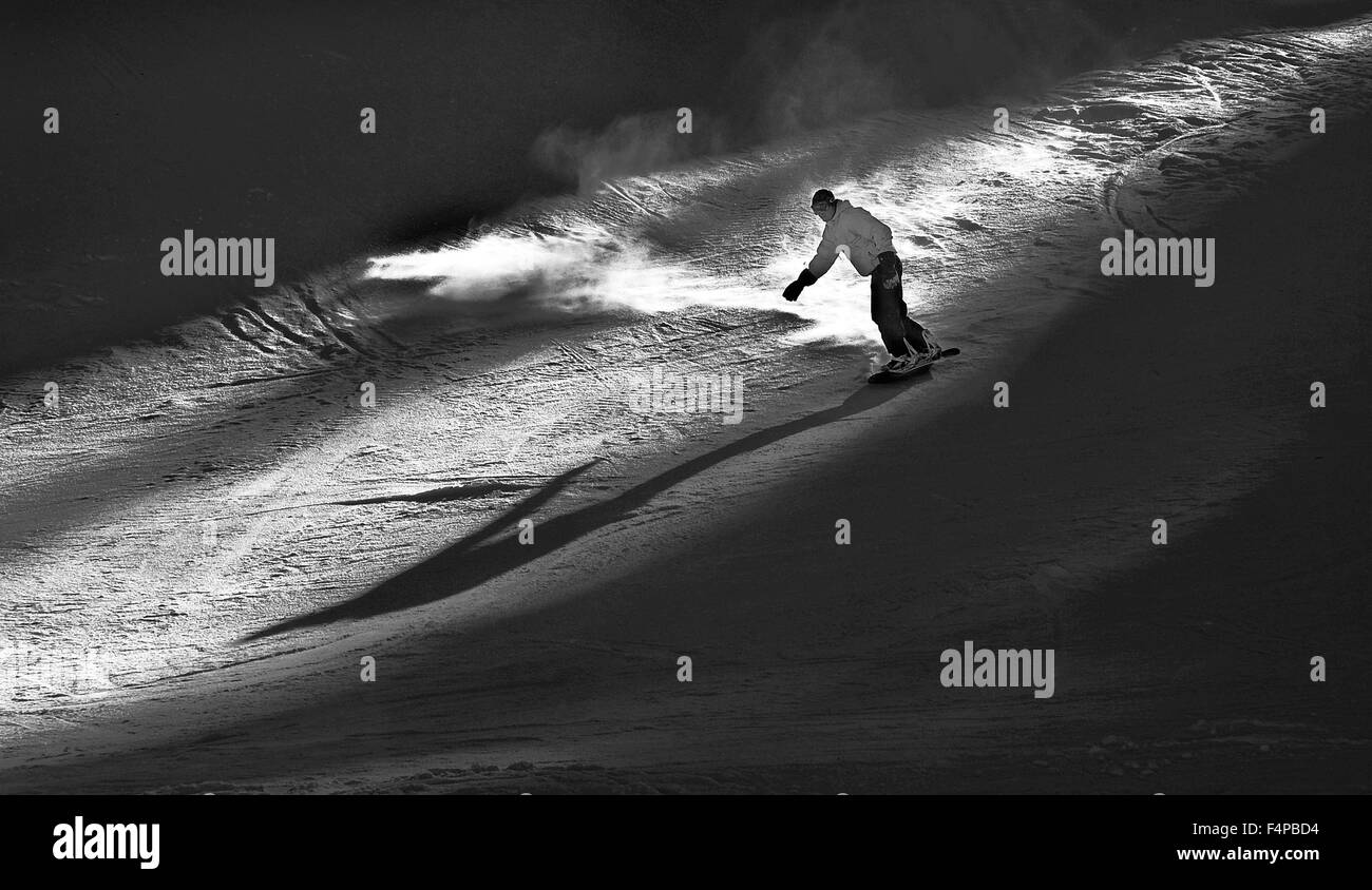 Mono image of snowboarder descending in shaft of sunlight. Stock Photo