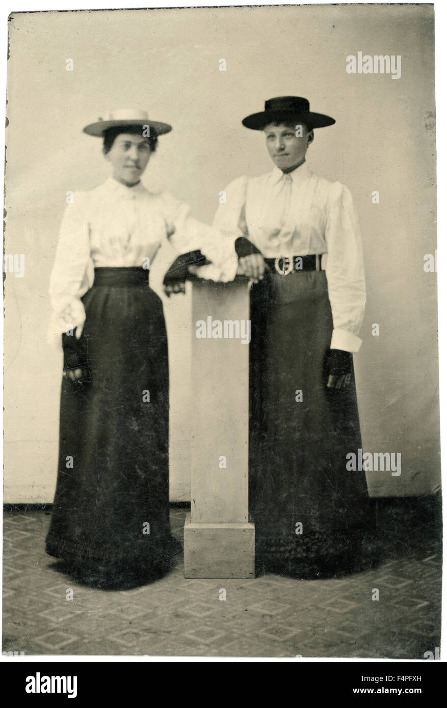 Portrait of Two Adult Women in Hats and Long Dresses Leaning on Pillar, circa 1870 Stock Photo