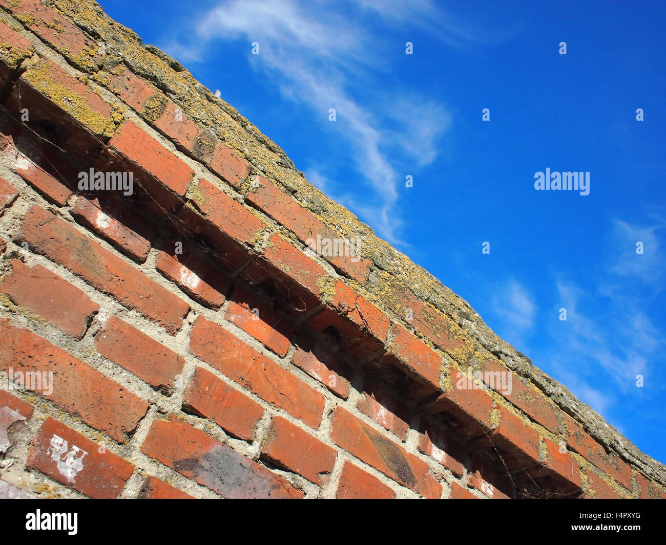 Bottom view on a fragment of an old brick fence against a bright blue sky with clouds on the diagonal of the frame. Stock Photo