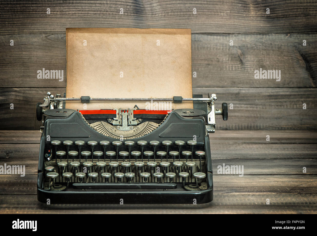 Antique typewriter with grungy worn paper page on wooden table. Vintage style toned picture Stock Photo