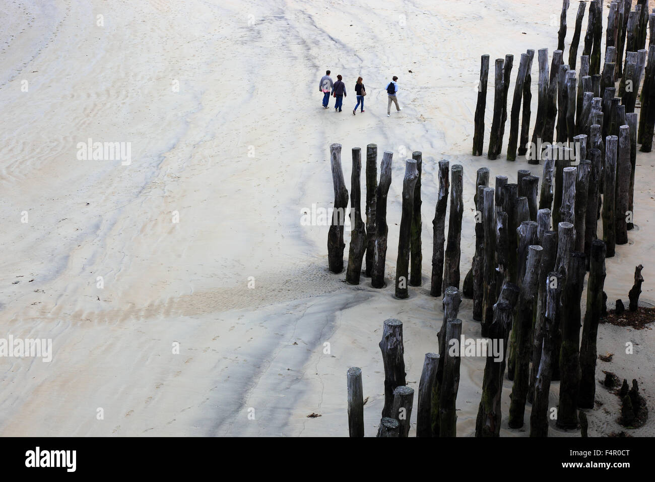 France, Brittany, Saint Malo, People walking at low tide walk on the sandy beach, wooden poles stuck in the sand, lined up in ro Stock Photo