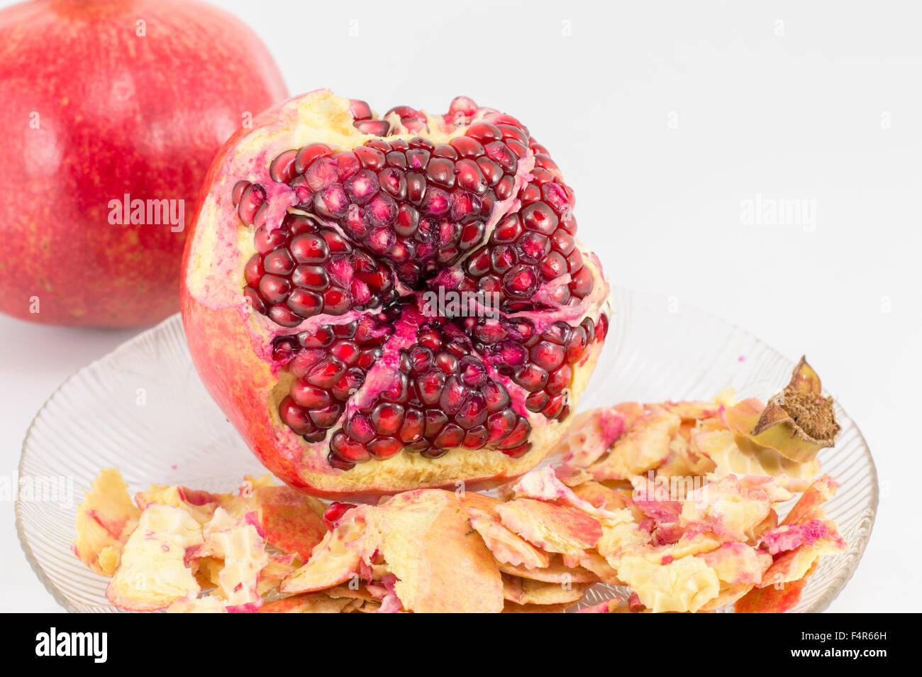 Juicy pomegranate partially peeled on a plate on white background Stock Photo