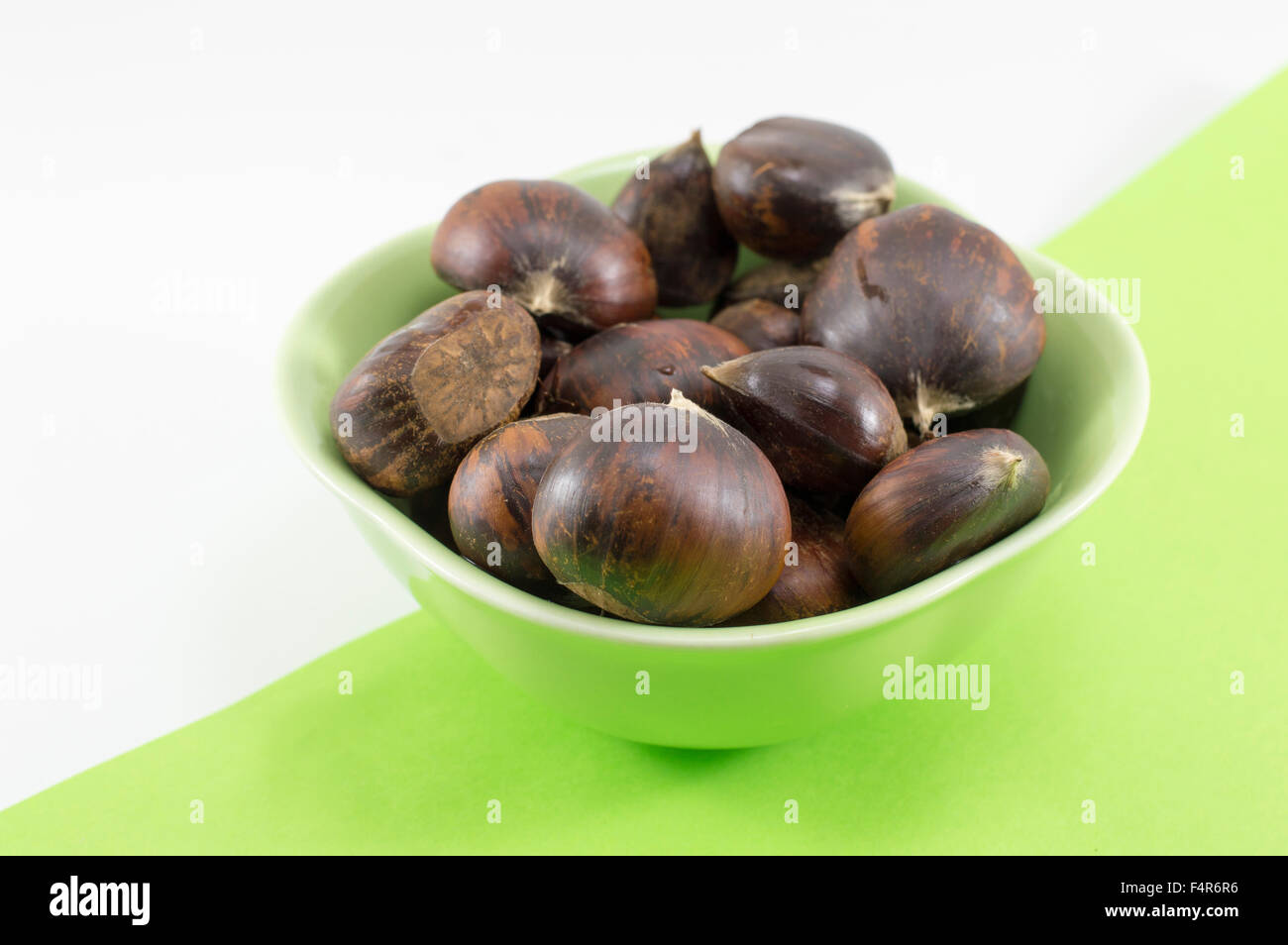 Fresh chestnuts in a green bowl on two colors background Stock Photo