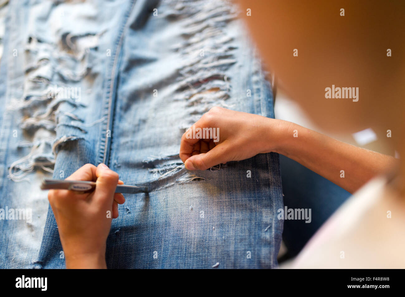 young girl is cutting her jeans (MR) Stock Photo