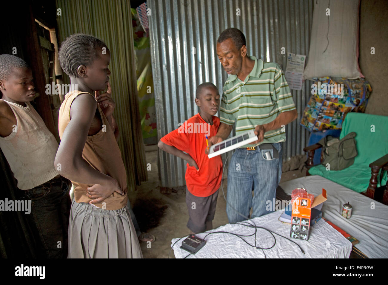 Teacher explaining PV panel and solar light to African children inside corrugated metal house Kamere Lake Naivasha Kenya Stock Photo