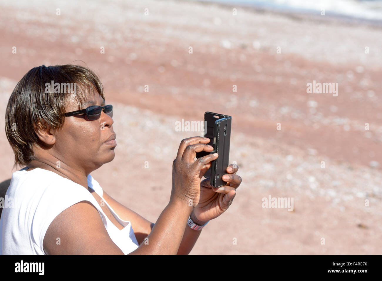 Woman taking holiday memento photos on her mobile phone of Oddicombe Beach, Torquay, Devon, England Stock Photo