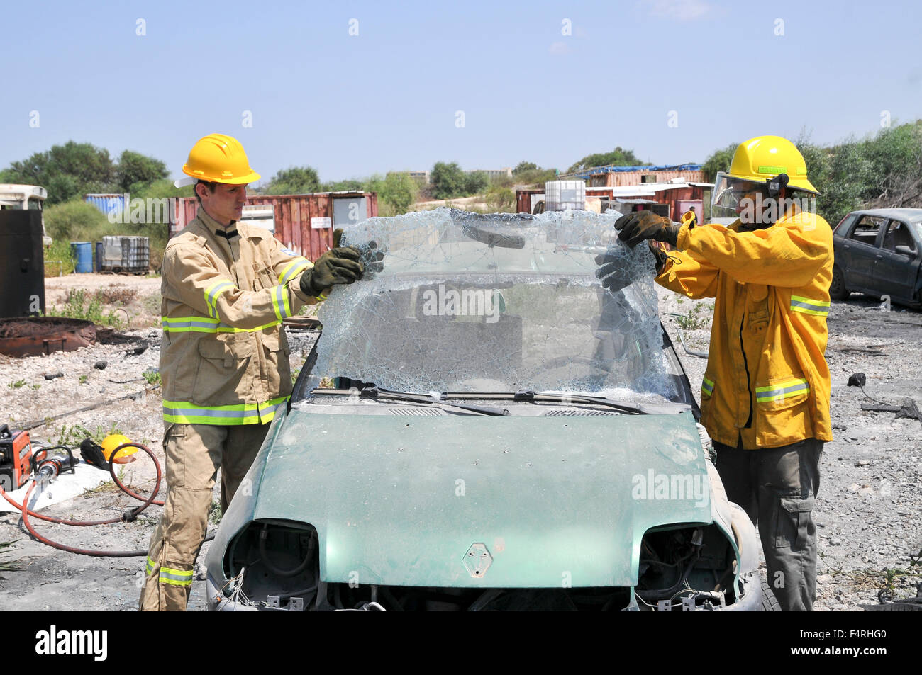 Firefighter uses an axe to break the front windshield of a car to rescue the trapped driver and passengers Stock Photo