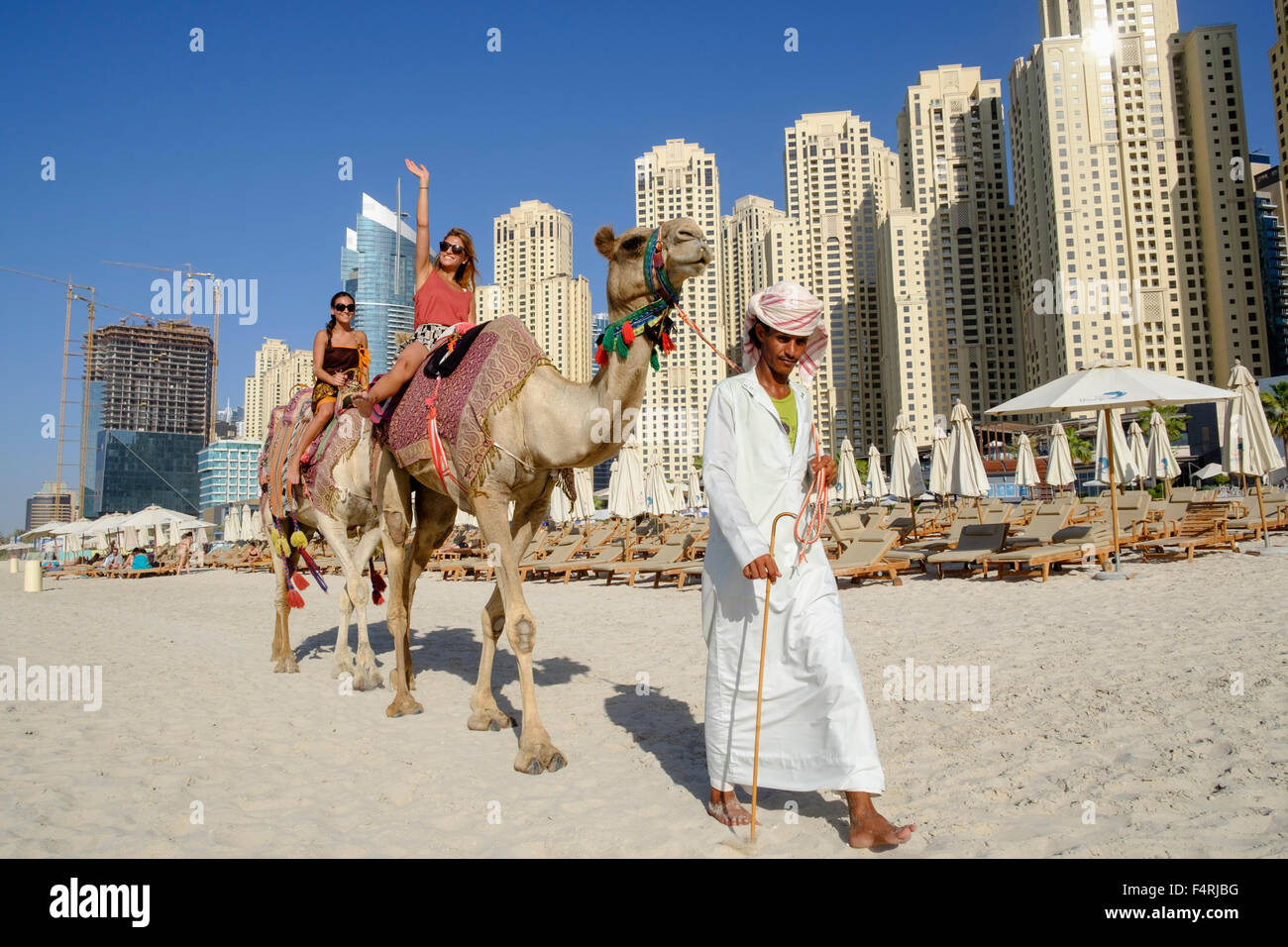 Tourists riding camel on beach at JBR Jumeirah Beach Residences in Marina district of Dubai United Arab Emirates Stock Photo