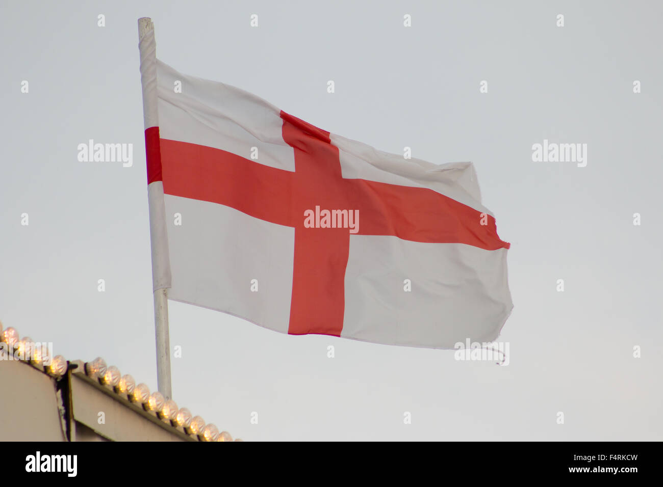 Flag of England (Saint George's Cross) fluttering on a flag pole. Grey sky. Stock Photo