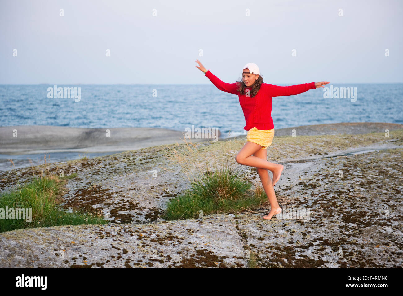 Girl (12-13) at seaside standing on one leg on rock Stock Photo