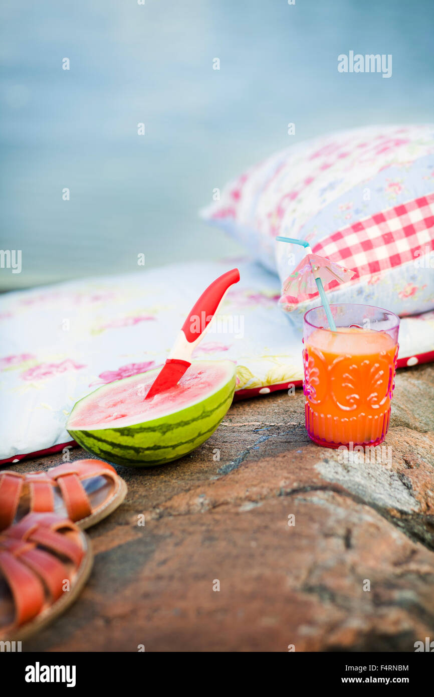 Sweden, Pillow, sandals, watermelon and glass of juice on rock Stock Photo