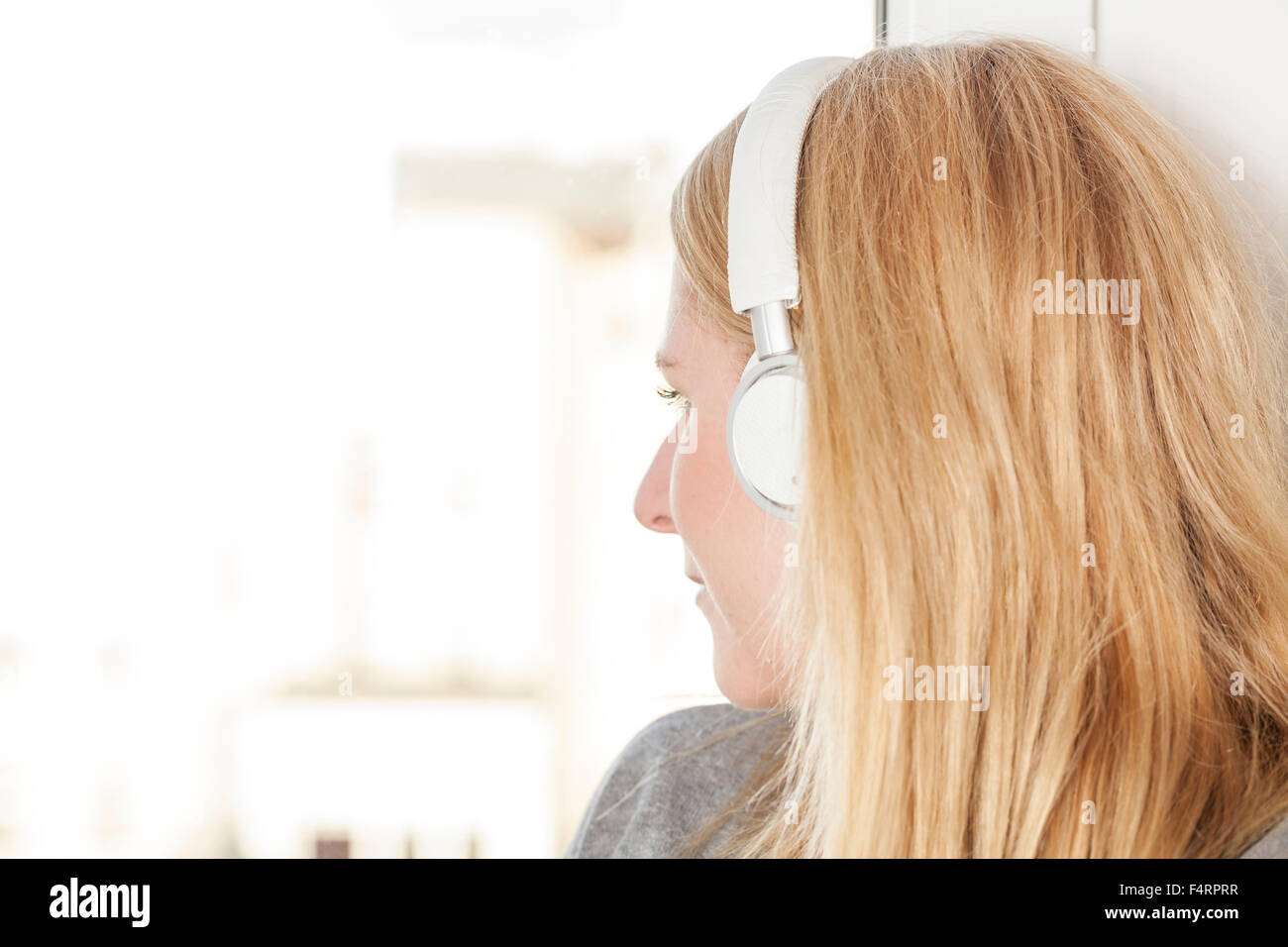 blond woman on window sill with headphones Stock Photo