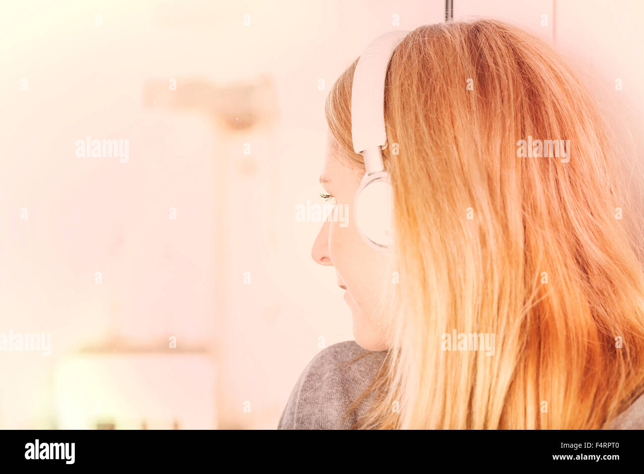blond woman with headphones on window sill Stock Photo