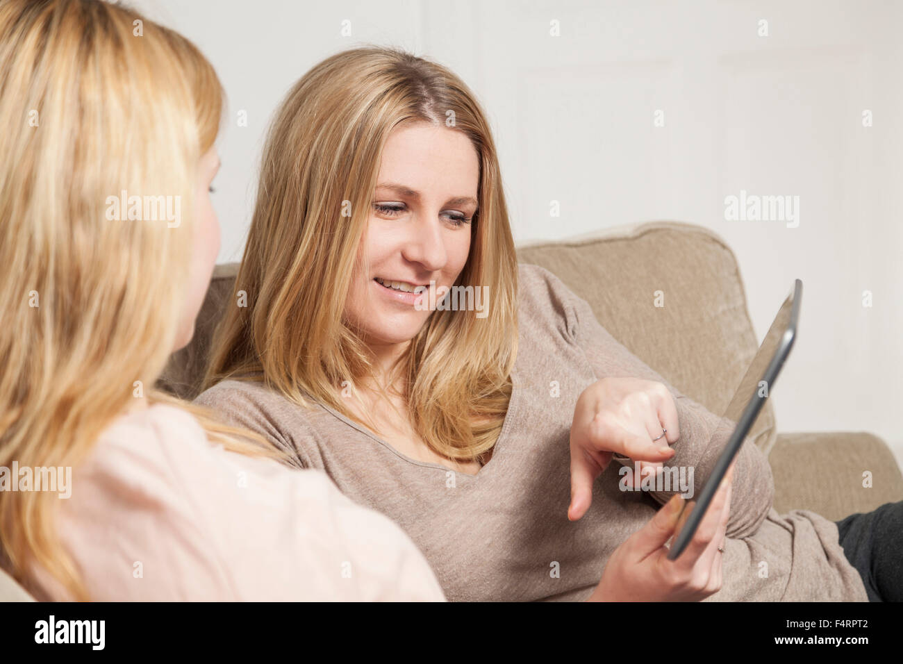 two blond womans on sofa looking at tablet computer Stock Photo