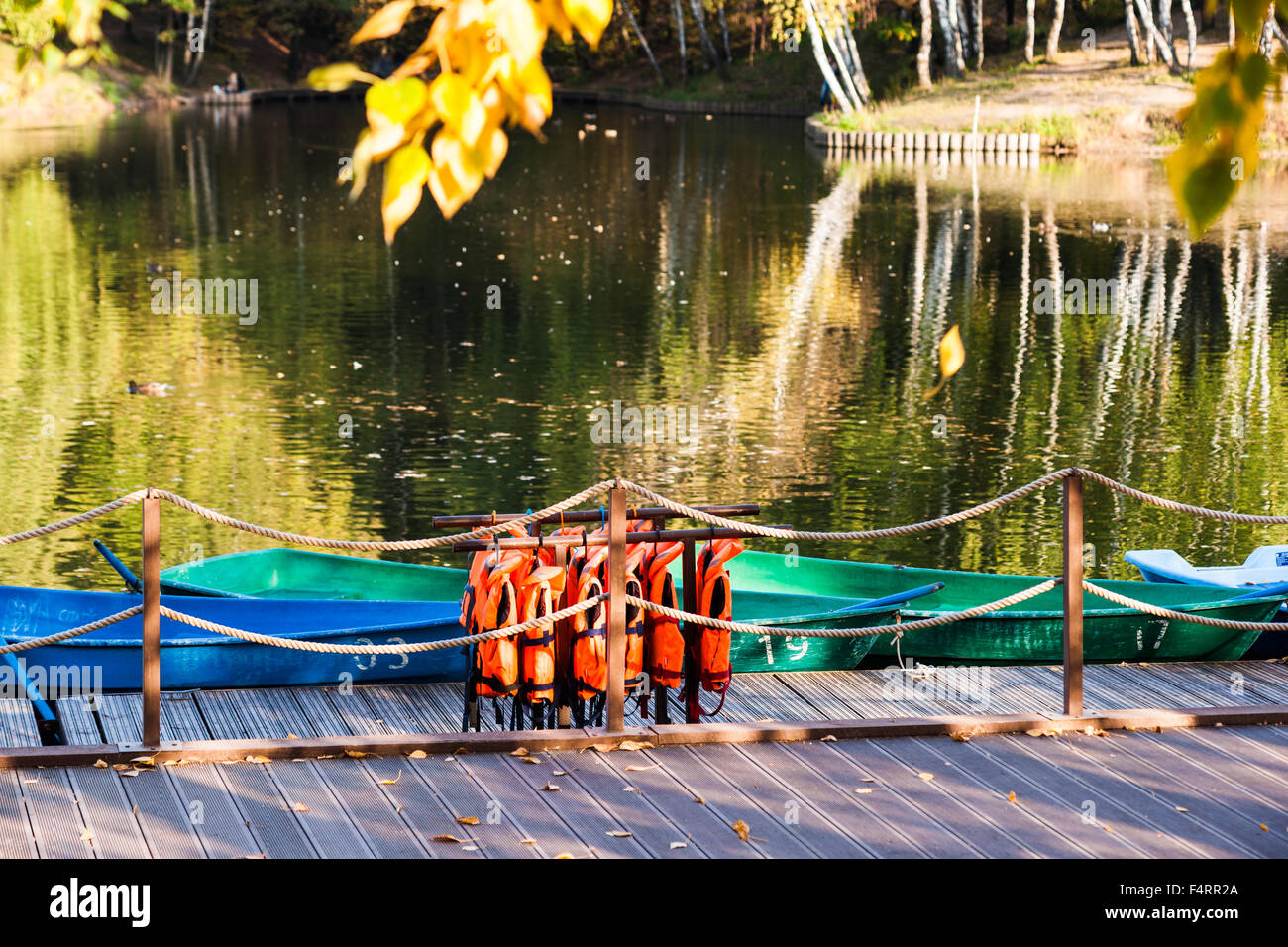Landing stage and a row of rental boats in autumn. Life-jackets hangs from a rail. Yellow leaf in the air. Nobody around. Stock Photo
