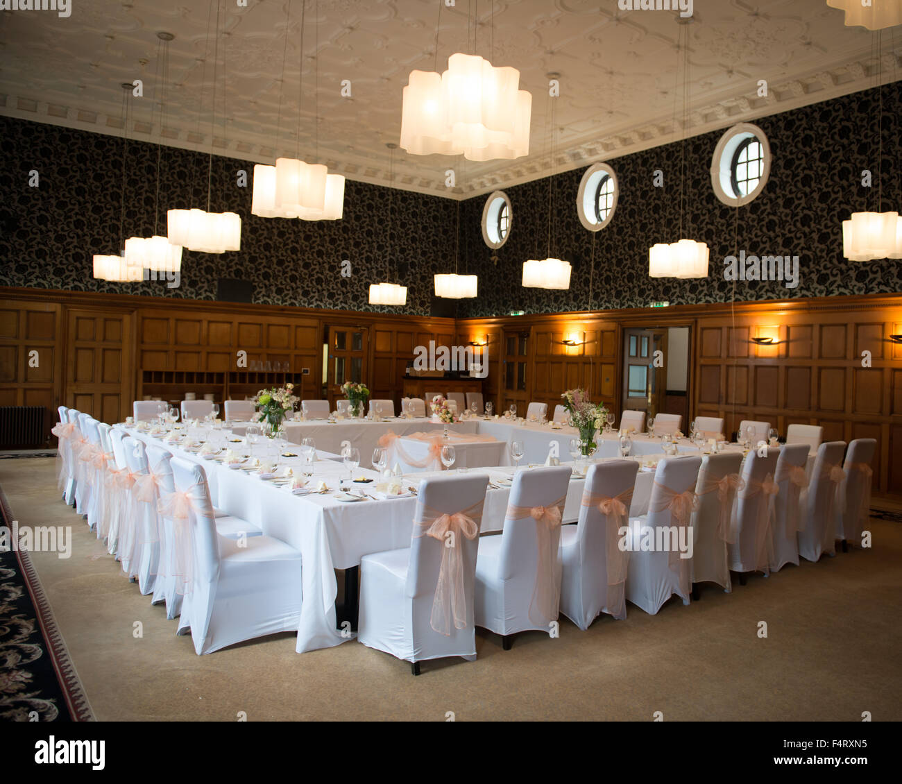 wedding reception room table layout tables set in a square formation with the cake in the centre white chair covers peach bows Stock Photo