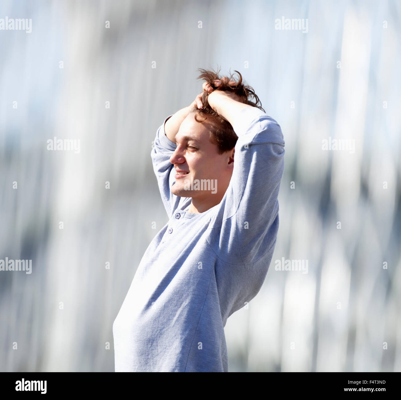 Young Man Standing, Fingers in Hair, Feeling Happy Stock Photo