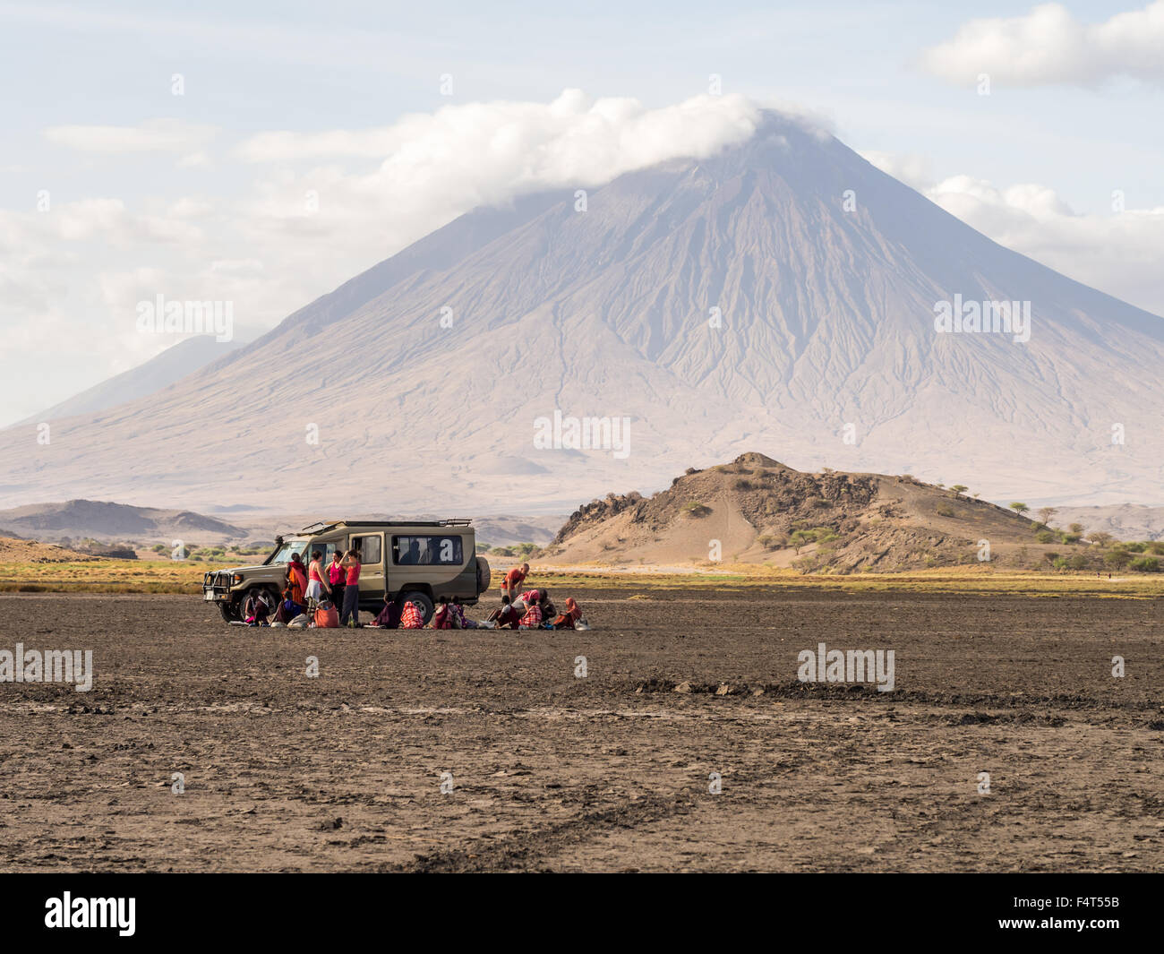 Maasai people sell their products to a tourist group in the dry part of Lake Natron. Ol Doinyo Lengai volcano in the background Stock Photo