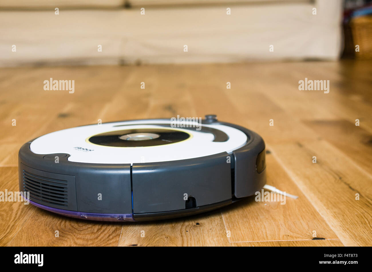 An iRobot Roomba robotic vacuum cleaner cleaning a wooden living room floor Stock Photo
