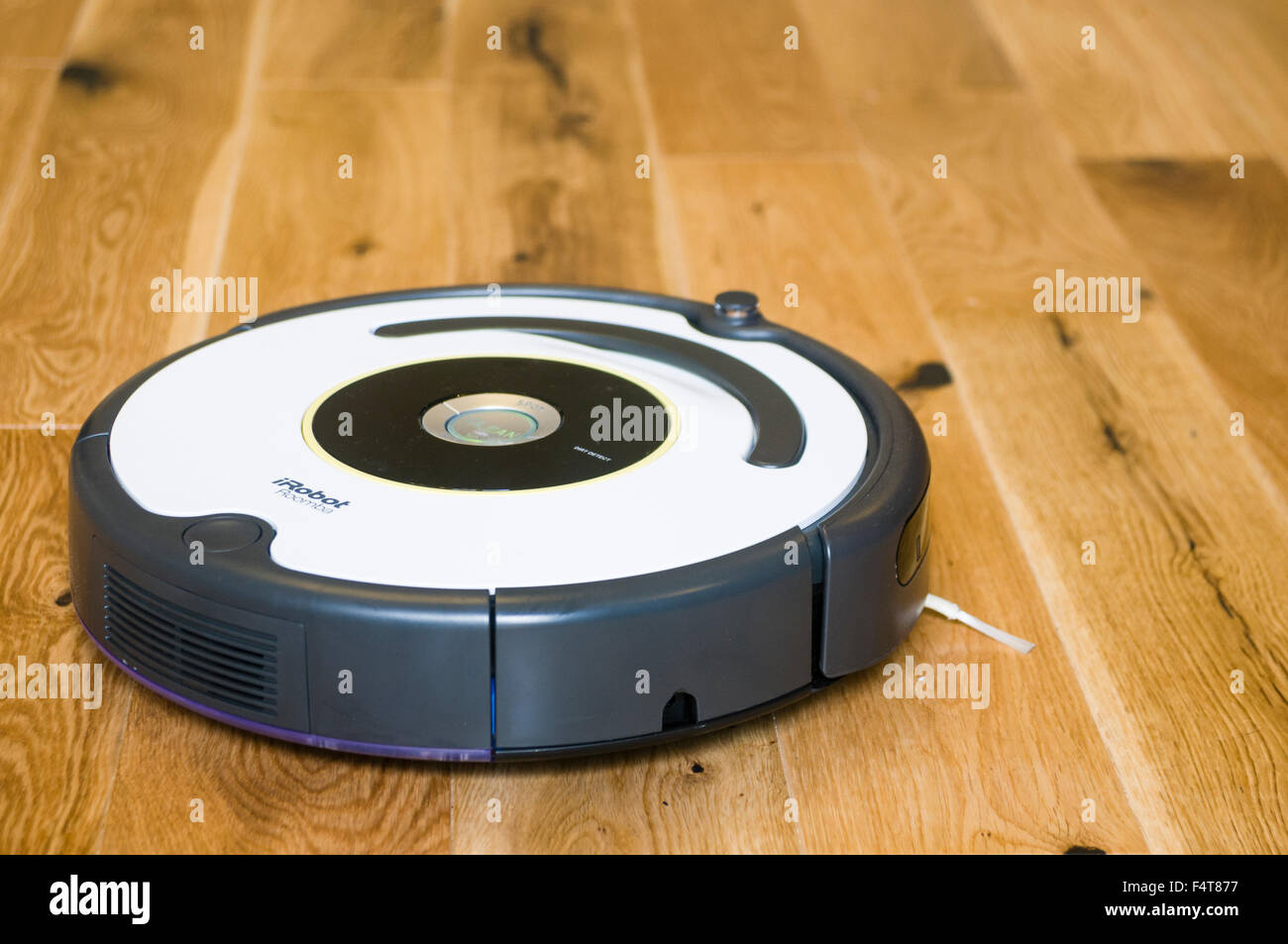 An iRobot Roomba robotic vacuum cleaner cleaning a wooden living room floor Stock Photo