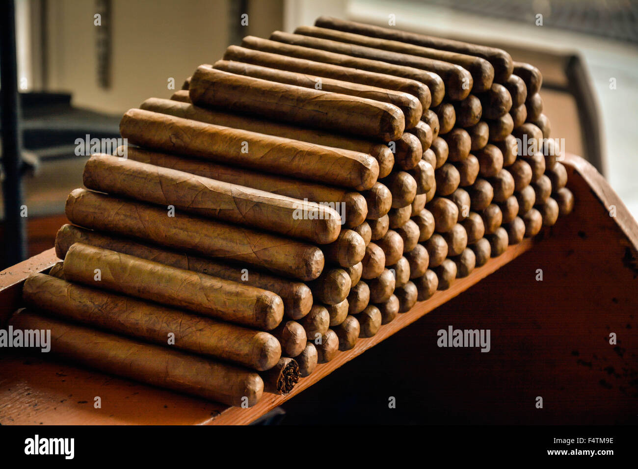 Moody, backlit and nostalgic view of Hand rolled Cuban cigars stacked in cigar factory work bench area Stock Photo