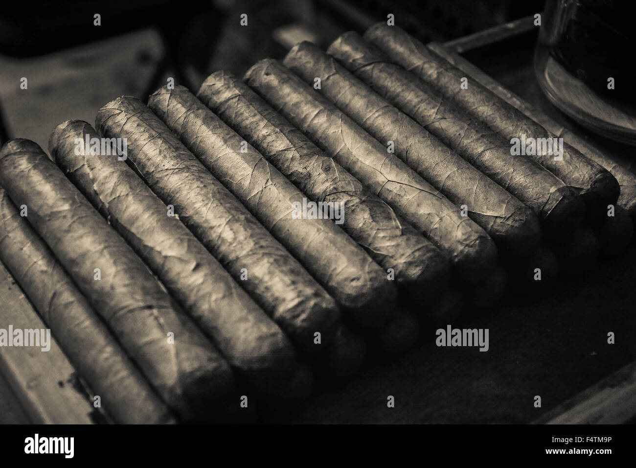Moody, artistic and nostalgic view of Hand rolled Cuban cigars stacked in cigar factory work bench area Stock Photo