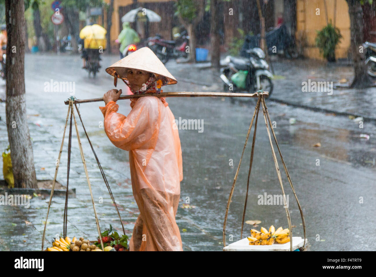 vietnamese female street food vendor with yoke and waterproof mac for rain showers,Hoi An,Vietnam Stock Photo