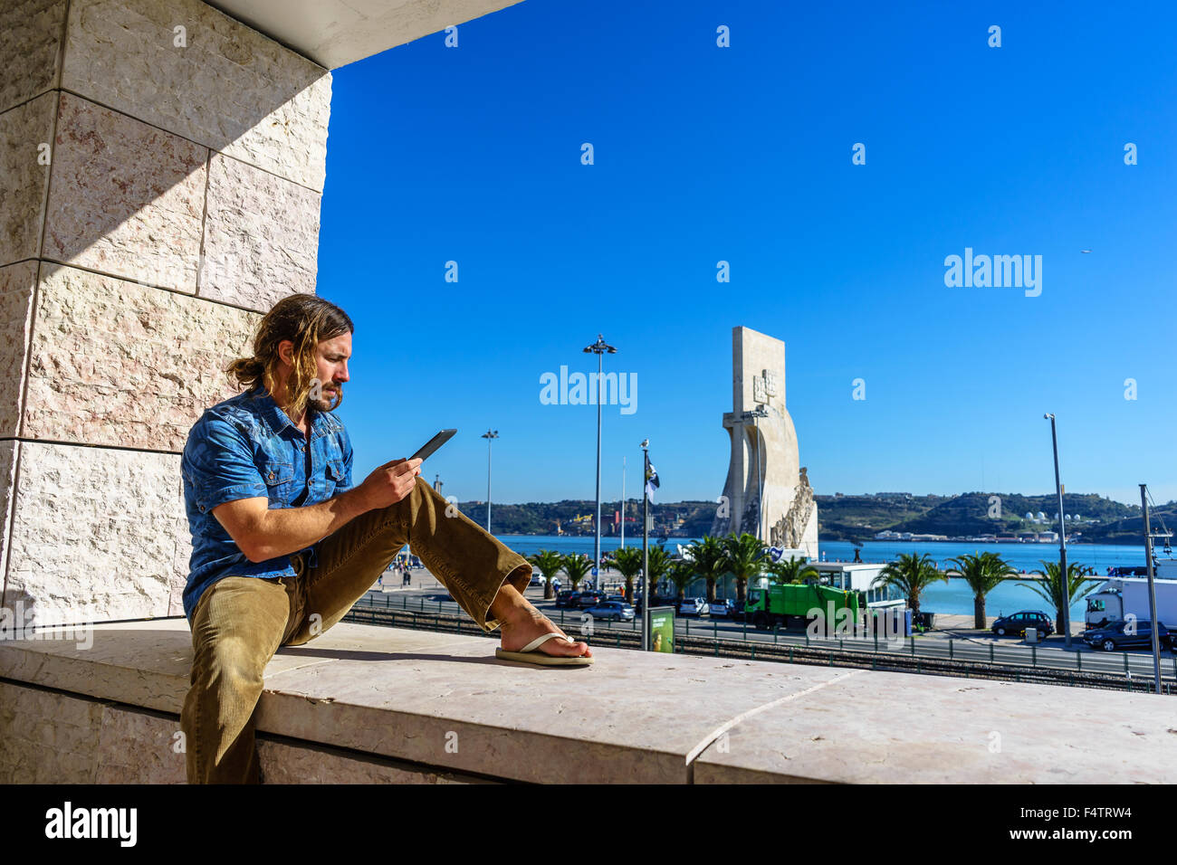 Man reads from an electronic tablet in front of the Portuguese icon, Monument to the Discoveries Padrao dos Descobrimentos. Stock Photo
