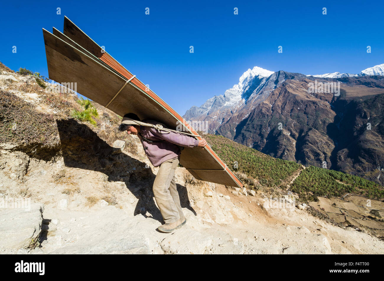 Porter carrying heavy load up an ascending track above Namche Bazar (3.440 m), the base for trekking and mountaineering in Solo Stock Photo