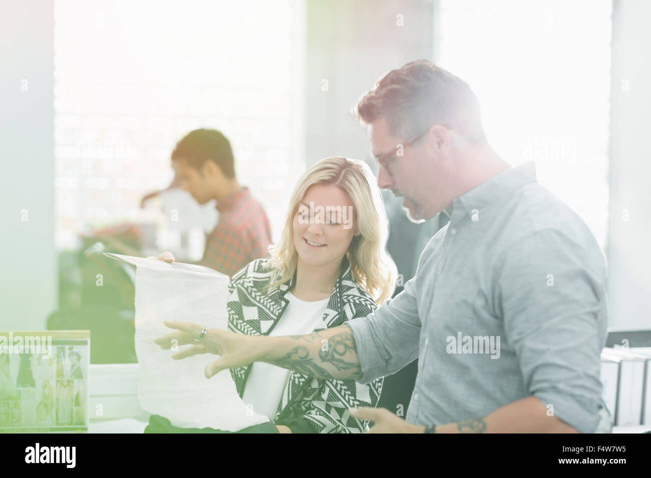 Fashion designers discussing fabric swatch in sunny office Stock Photo