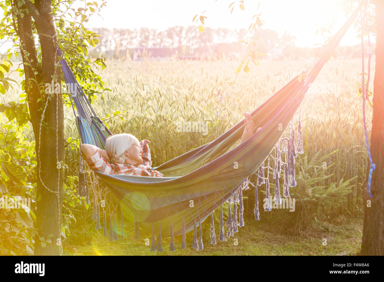 Serene woman napping in hammock next to sunny rural wheat field Stock Photo