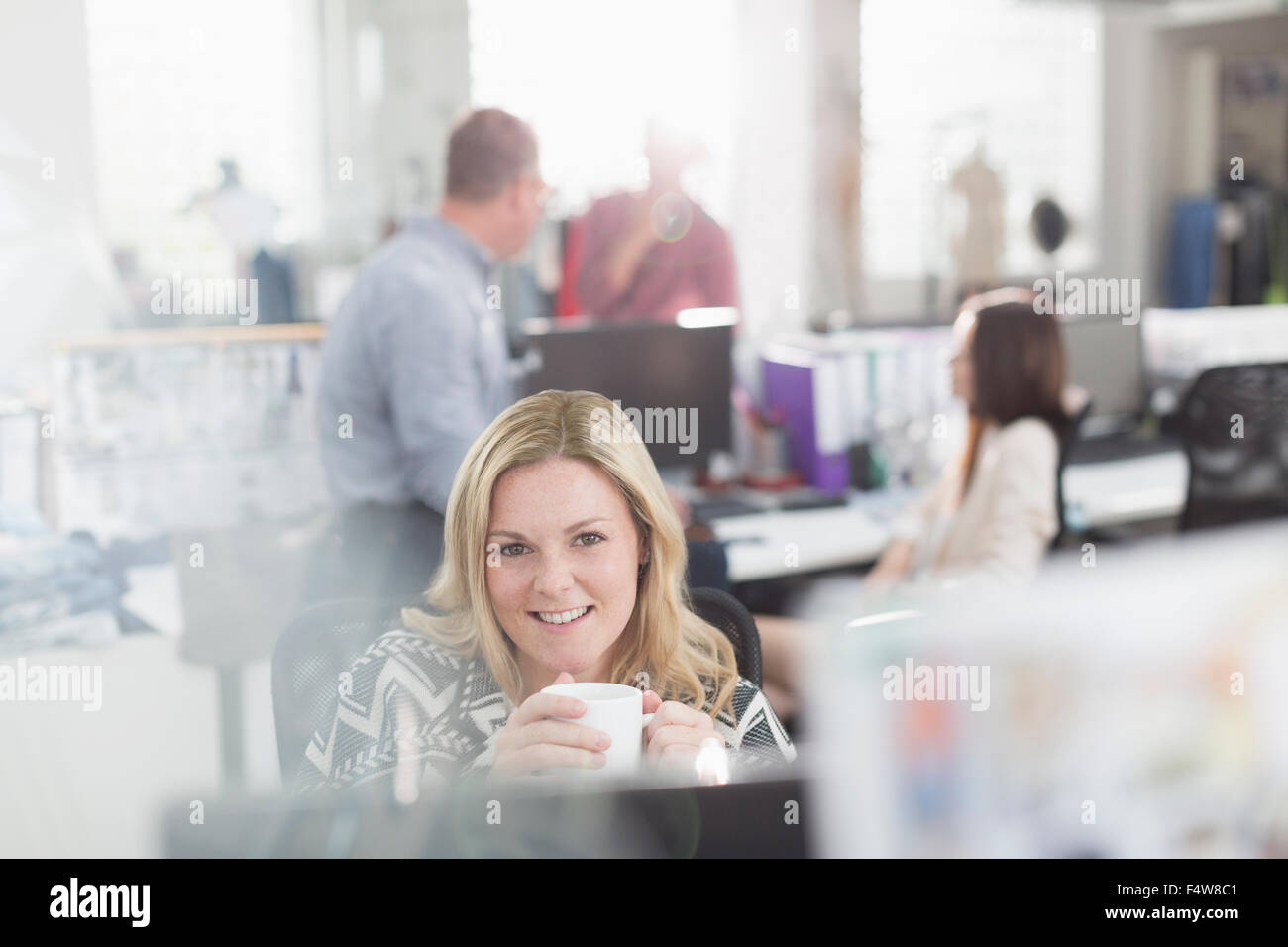 Portrait smiling fashion designer drinking coffee at computer in office Stock Photo