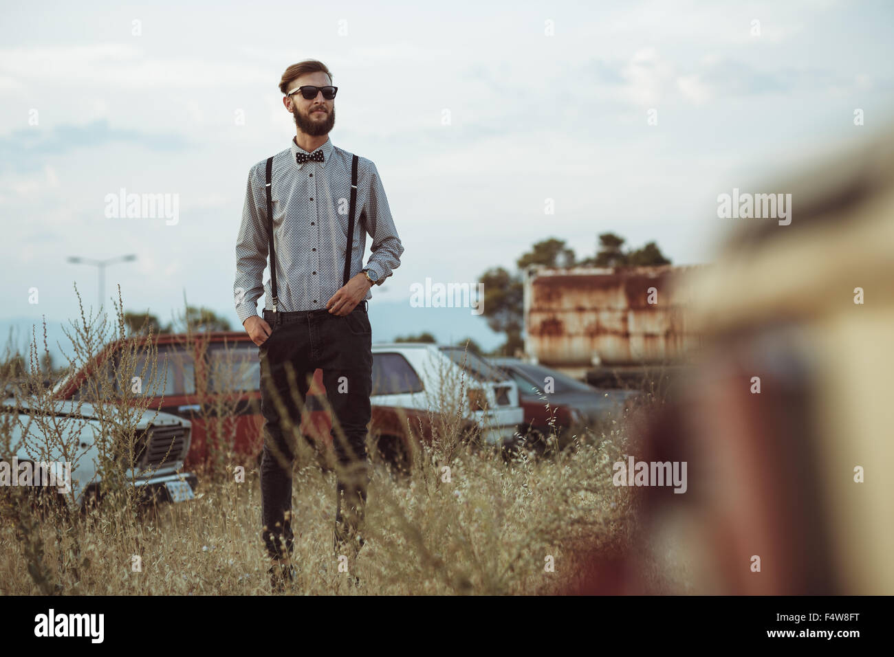 Portrait of a young handsome stylish man, wearing shirt and bow-tie on the field of old cars Stock Photo