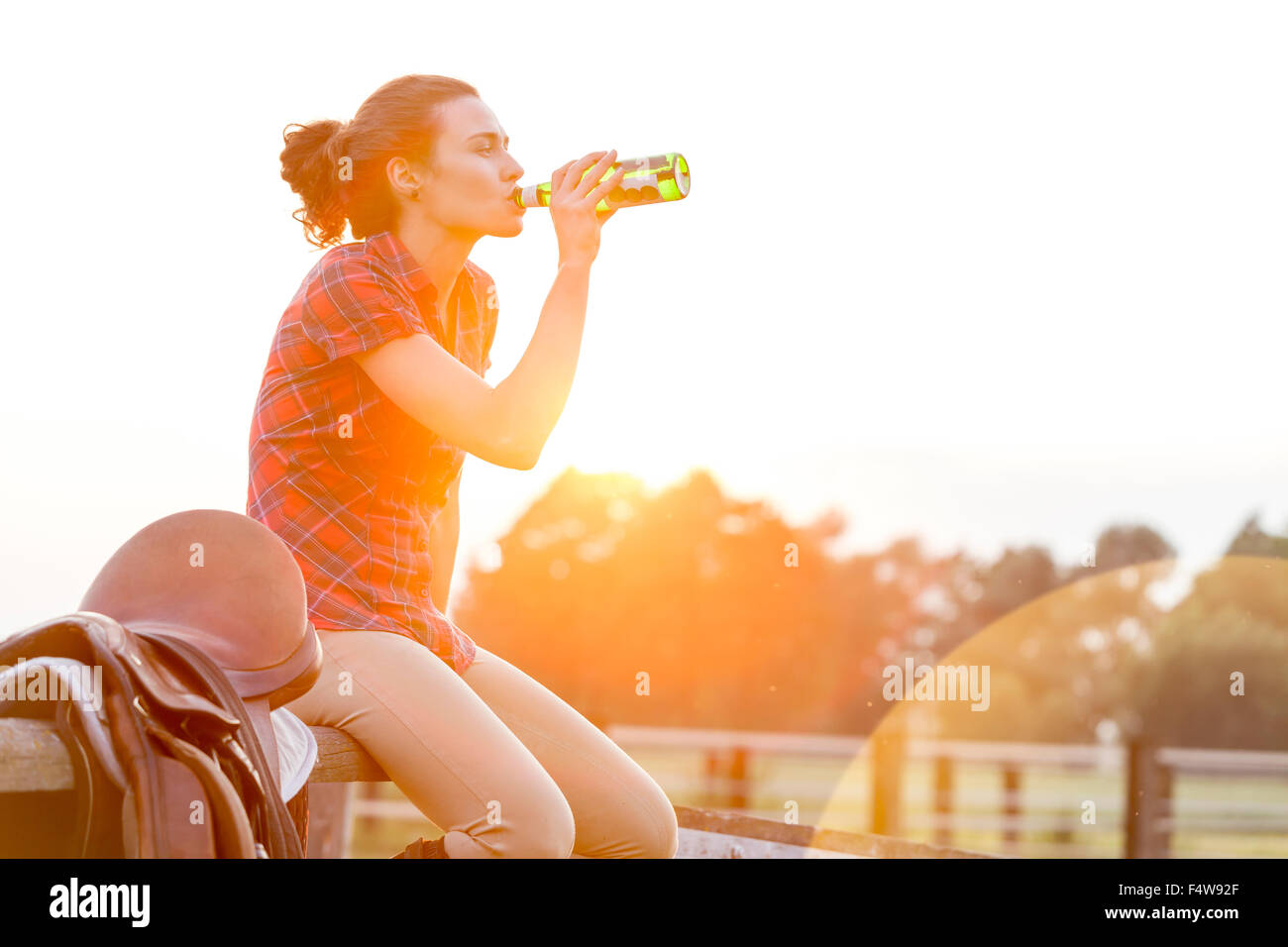 Woman drinking water next to saddle on rural fence Stock Photo
