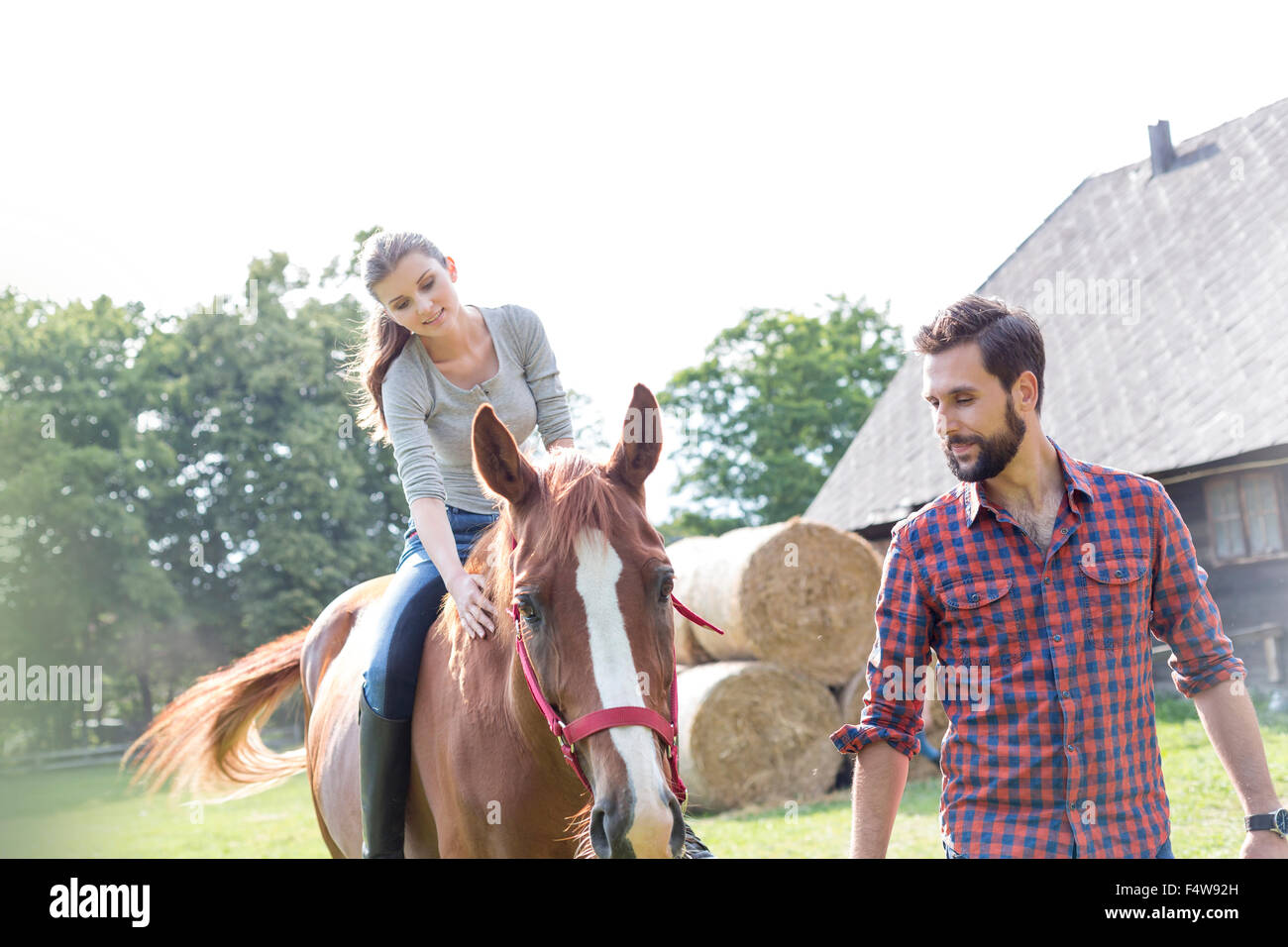 Man leading woman horseback riding in rural pasture Stock Photo