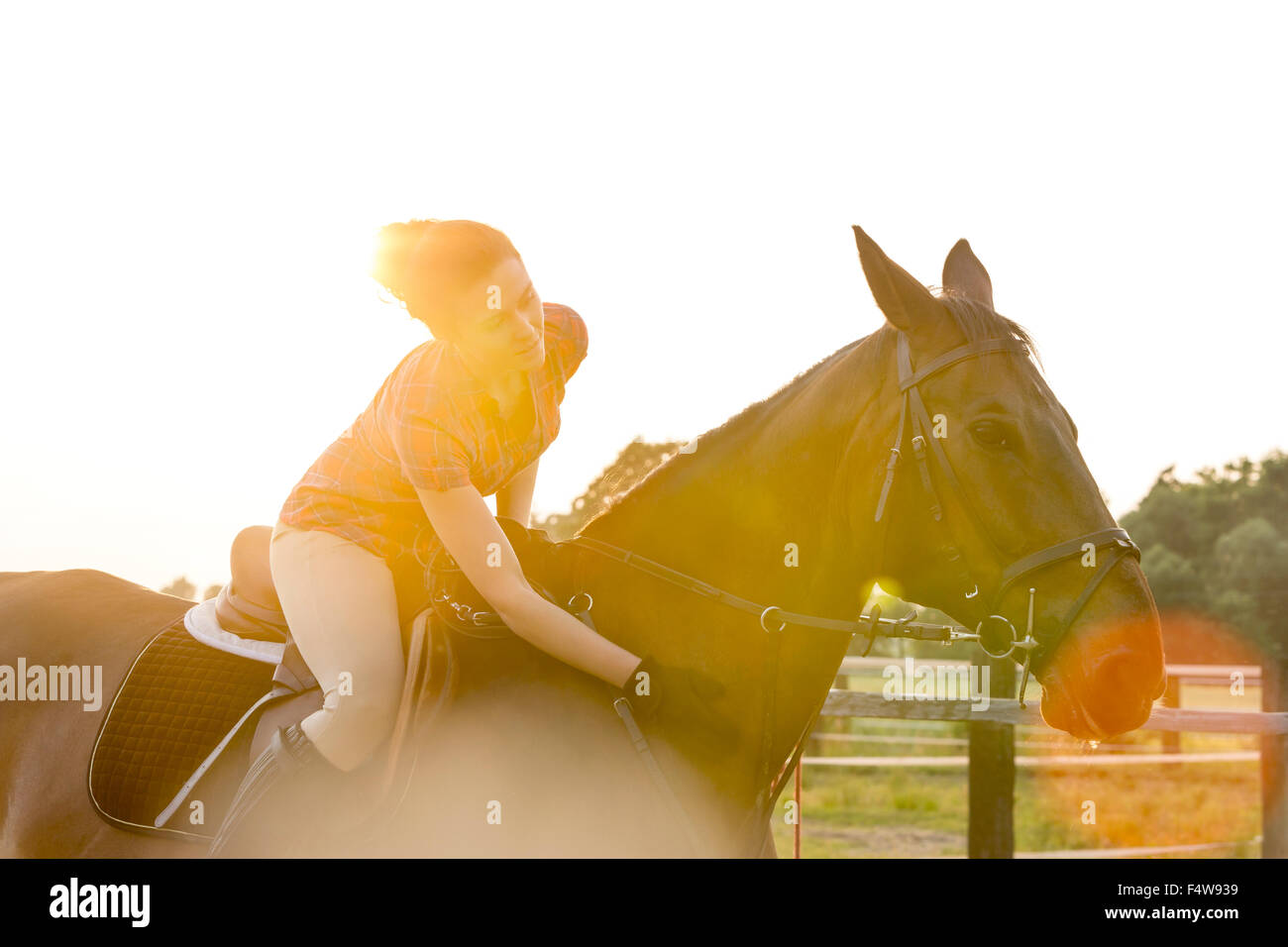 Woman on horseback petting horse in rural pasture Stock Photo