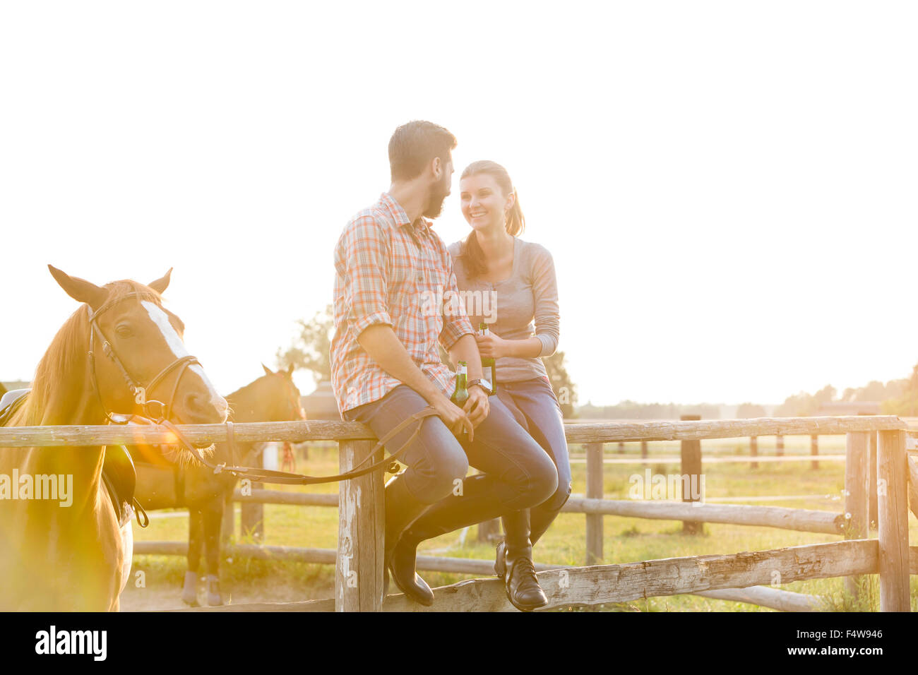 Couple with horse talking on sunny rural pasture fence Stock Photo