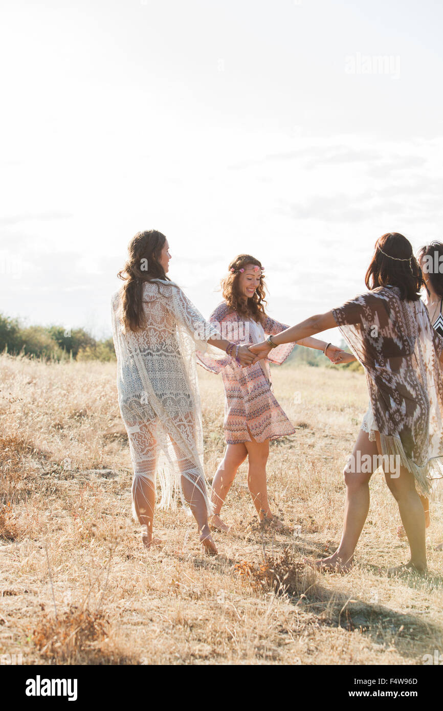 Boho women holding hands and dancing in circle in sunny rural field Stock Photo