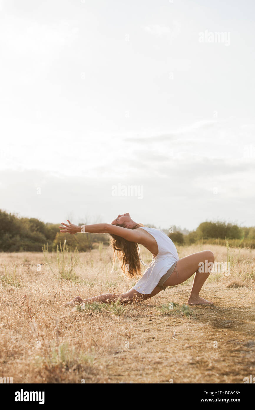 Boho woman in high crescent lunge yoga pose in sunny rural field Stock Photo