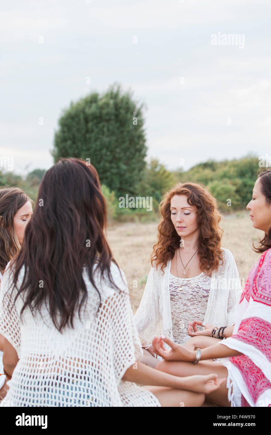 Boho women meditating in circle in rural field Stock Photo