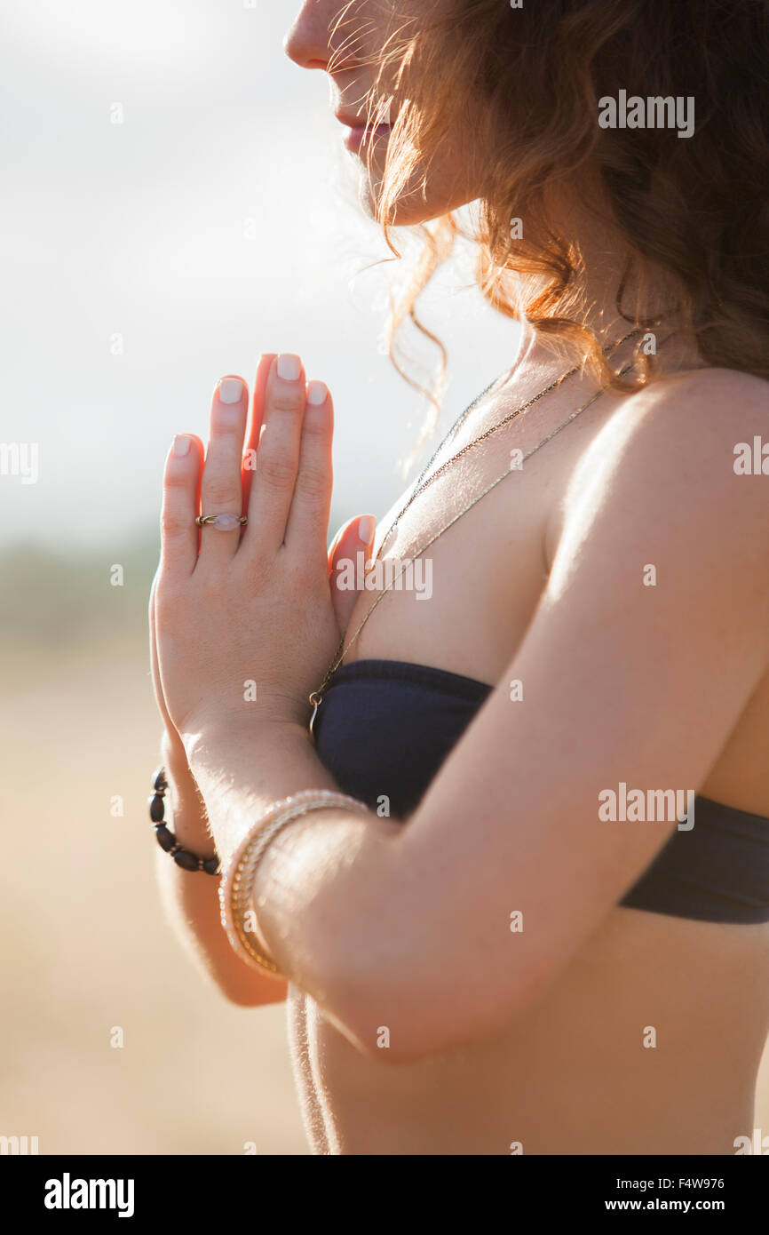 Close up serene woman in bikini meditating with hands at heart center Stock Photo