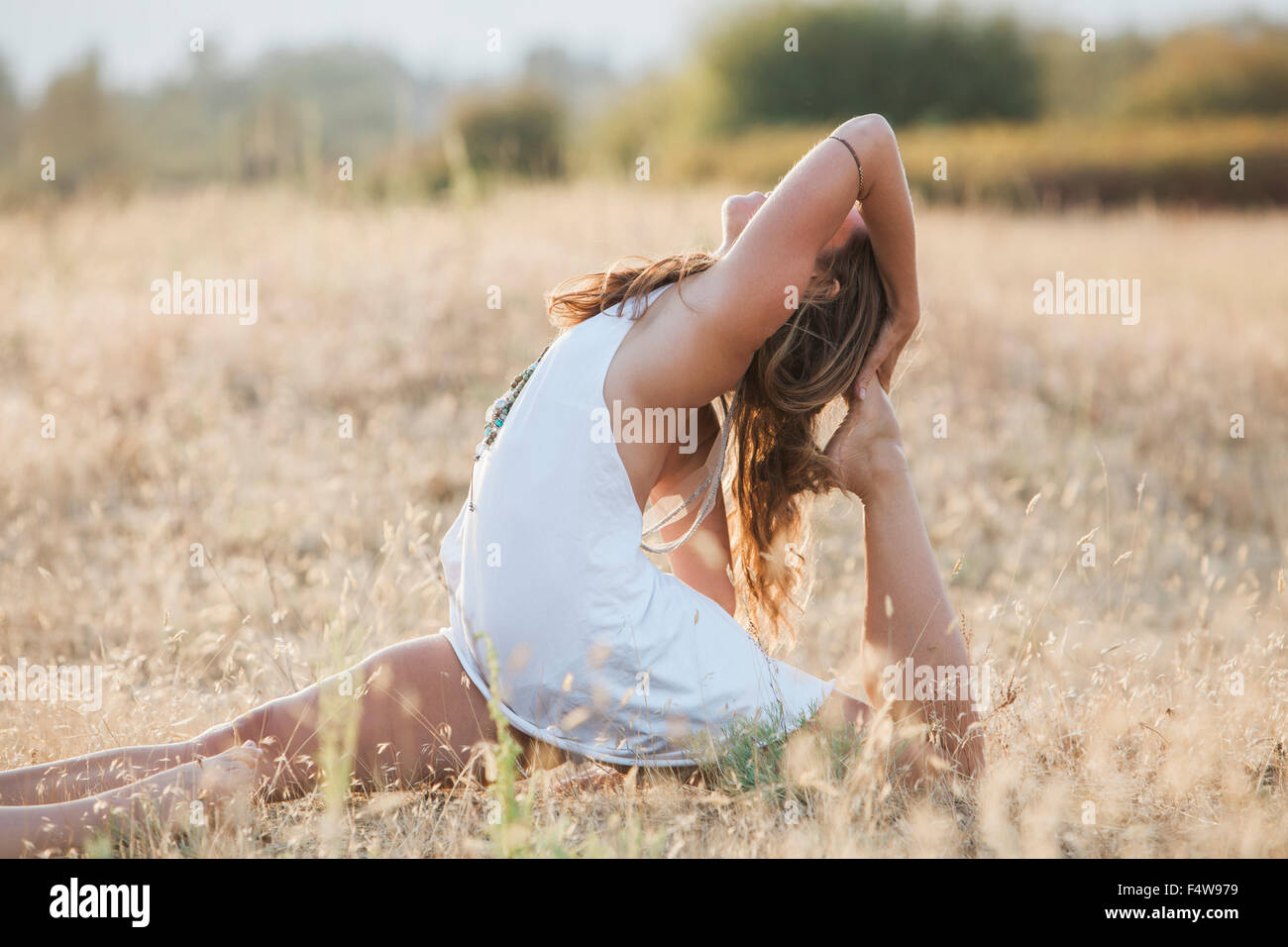 Boho woman in royal king pigeon pose in sunny rural field Stock Photo