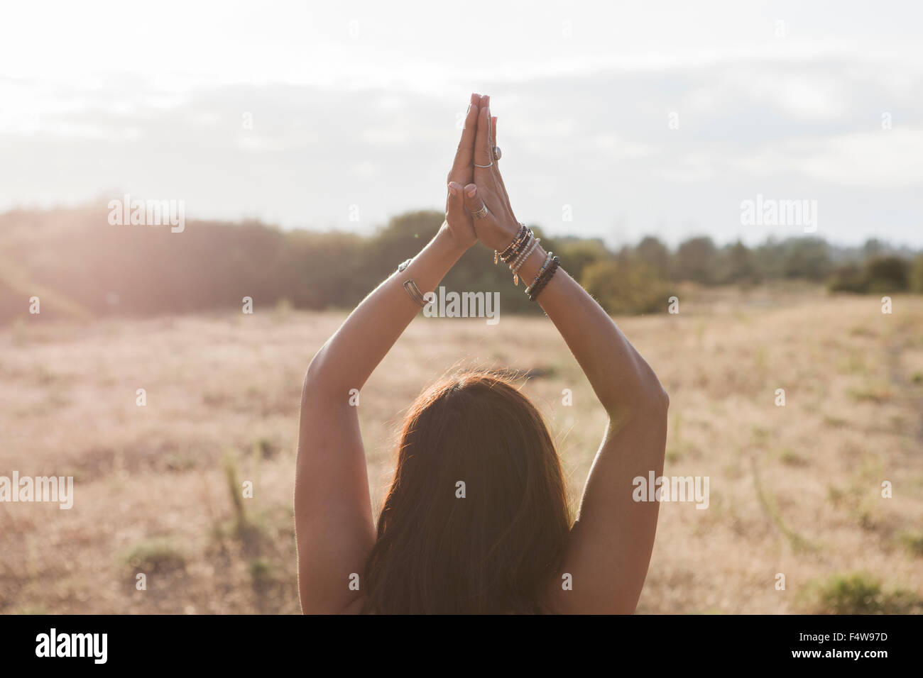 Woman meditating with hands clasped overhead in sunny rural field Stock Photo